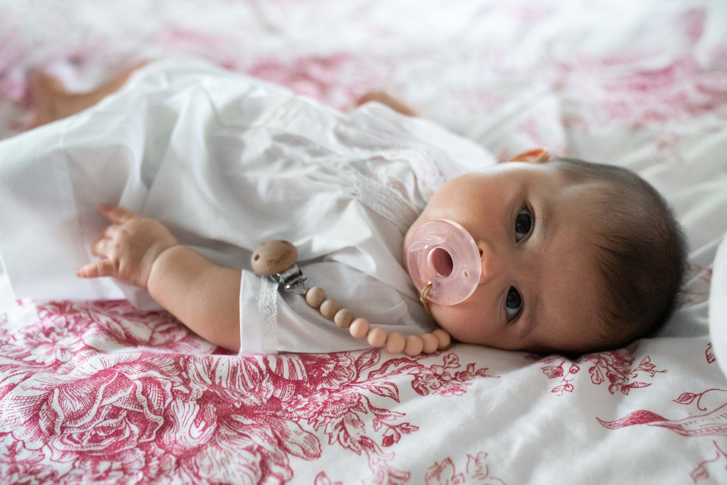 Baby dressed up and laying on bed with pacifier