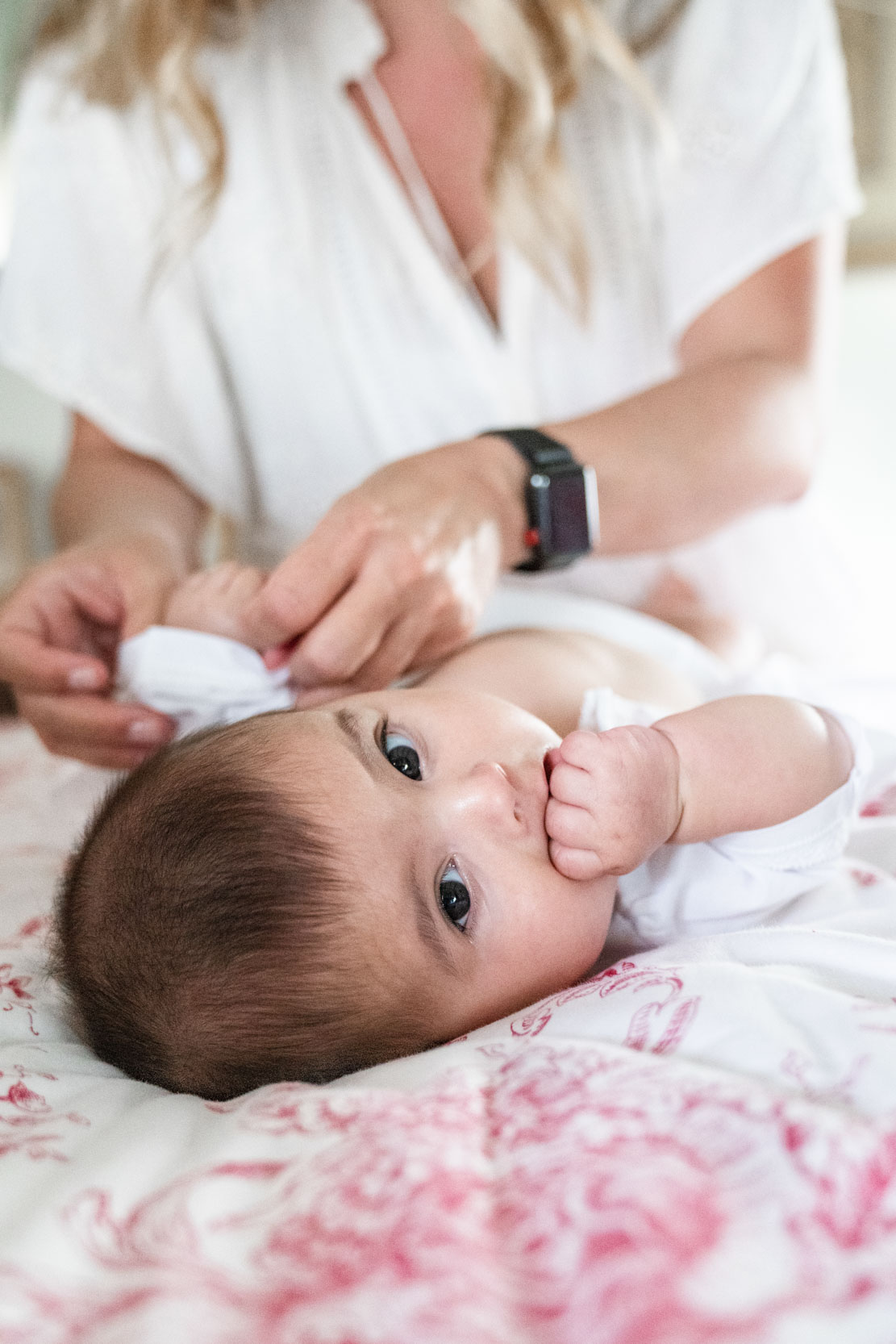 Baby sucking thumb while mother dresses baby