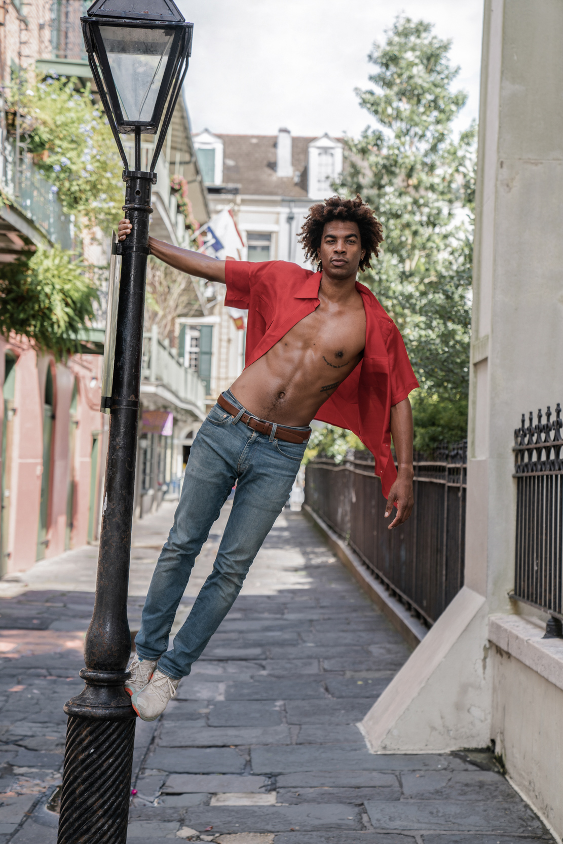 A shirtless dancer modeling and hanging from street post in the New Orleans French Quarter