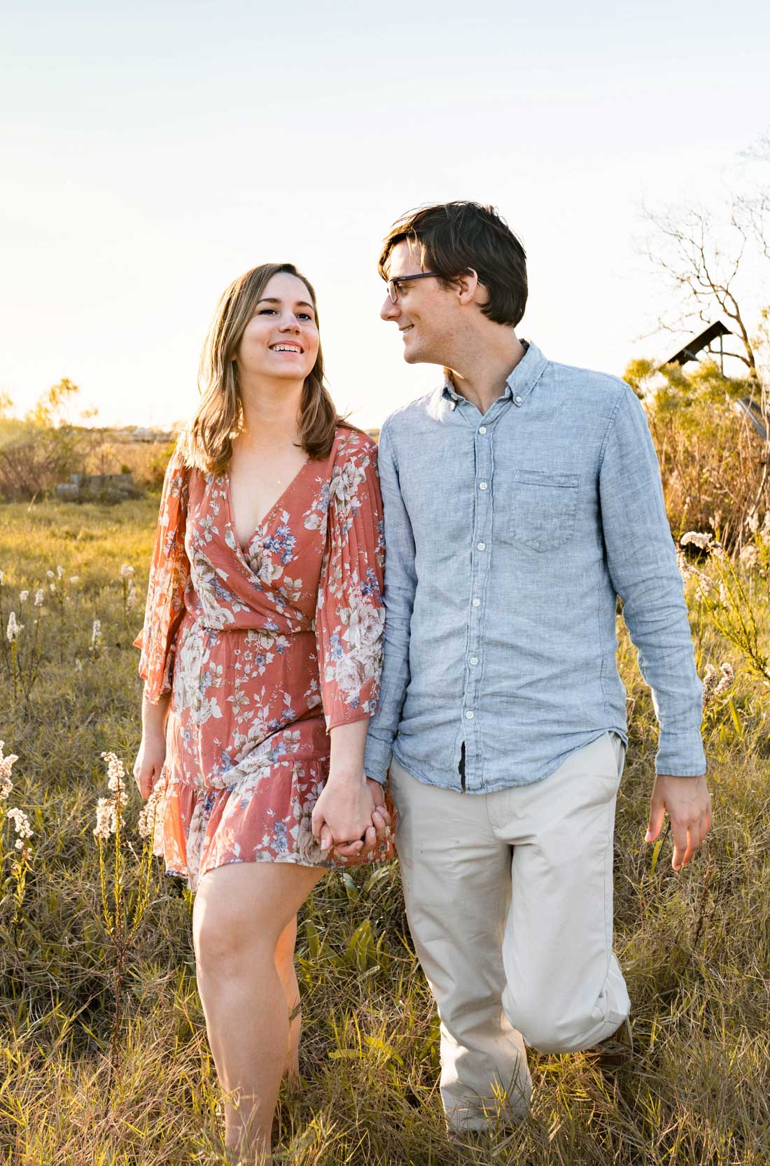 Happy couple walking in the grass along a Louisiana bayou at sunset after engagement proposal