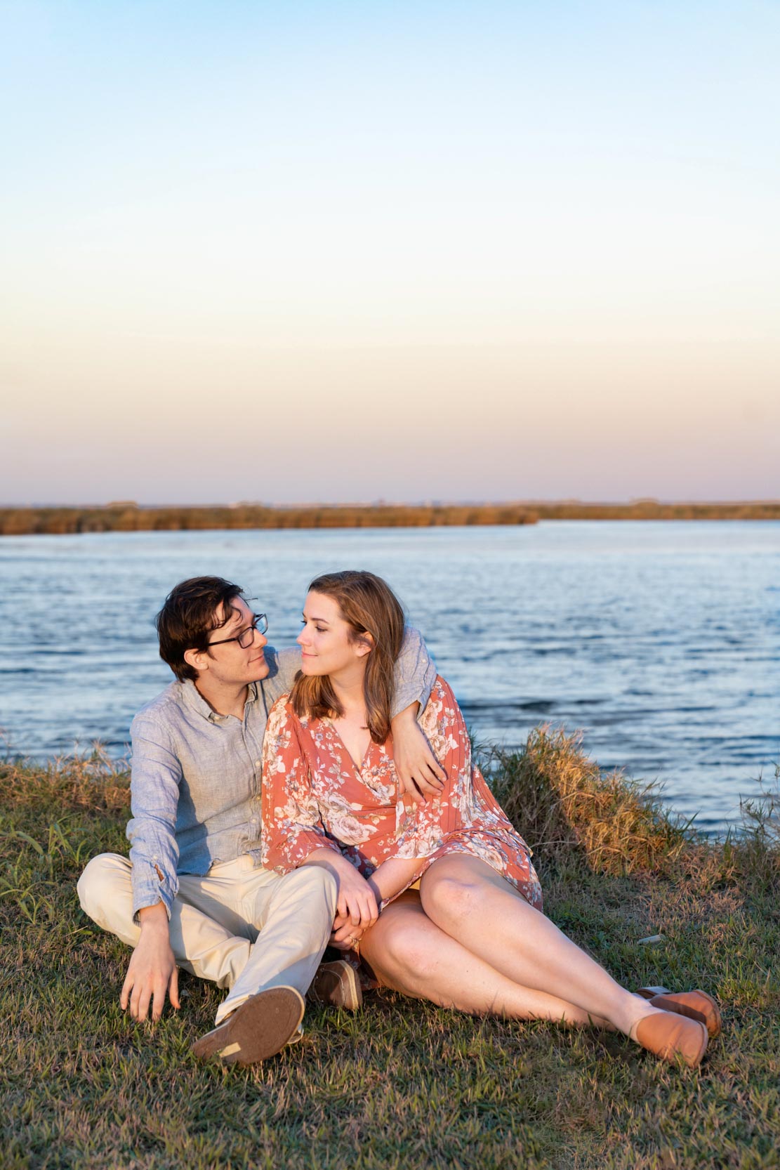 Couple sitting in the grass along a Louisiana bayou at sunset after engagement proposal