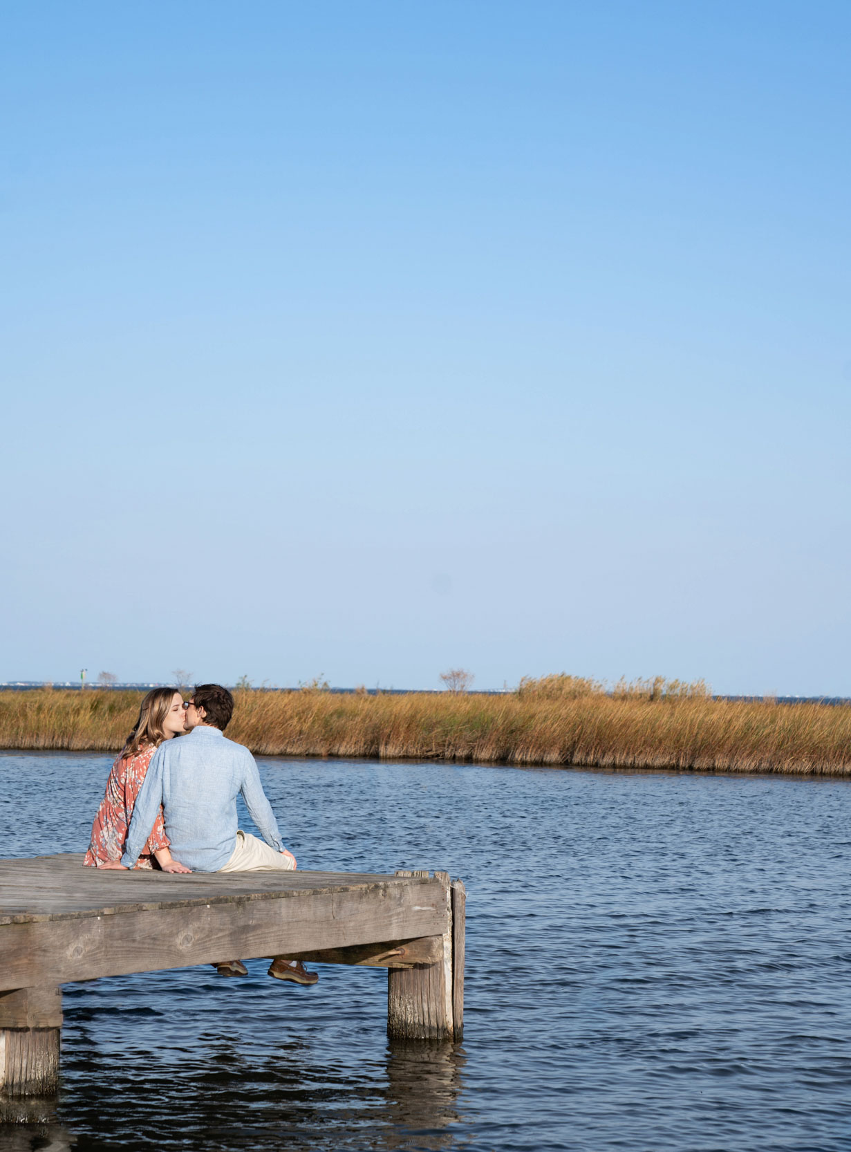 Engaged couple kissing and sitting on a bayou dock in Louisiana after engagement proposal