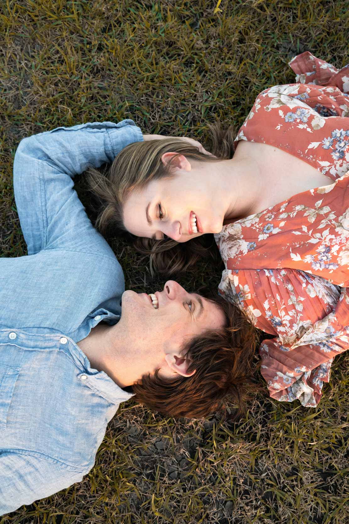 Couple smiling and lying in the grass along a bayou in Louisiana after engagement proposal