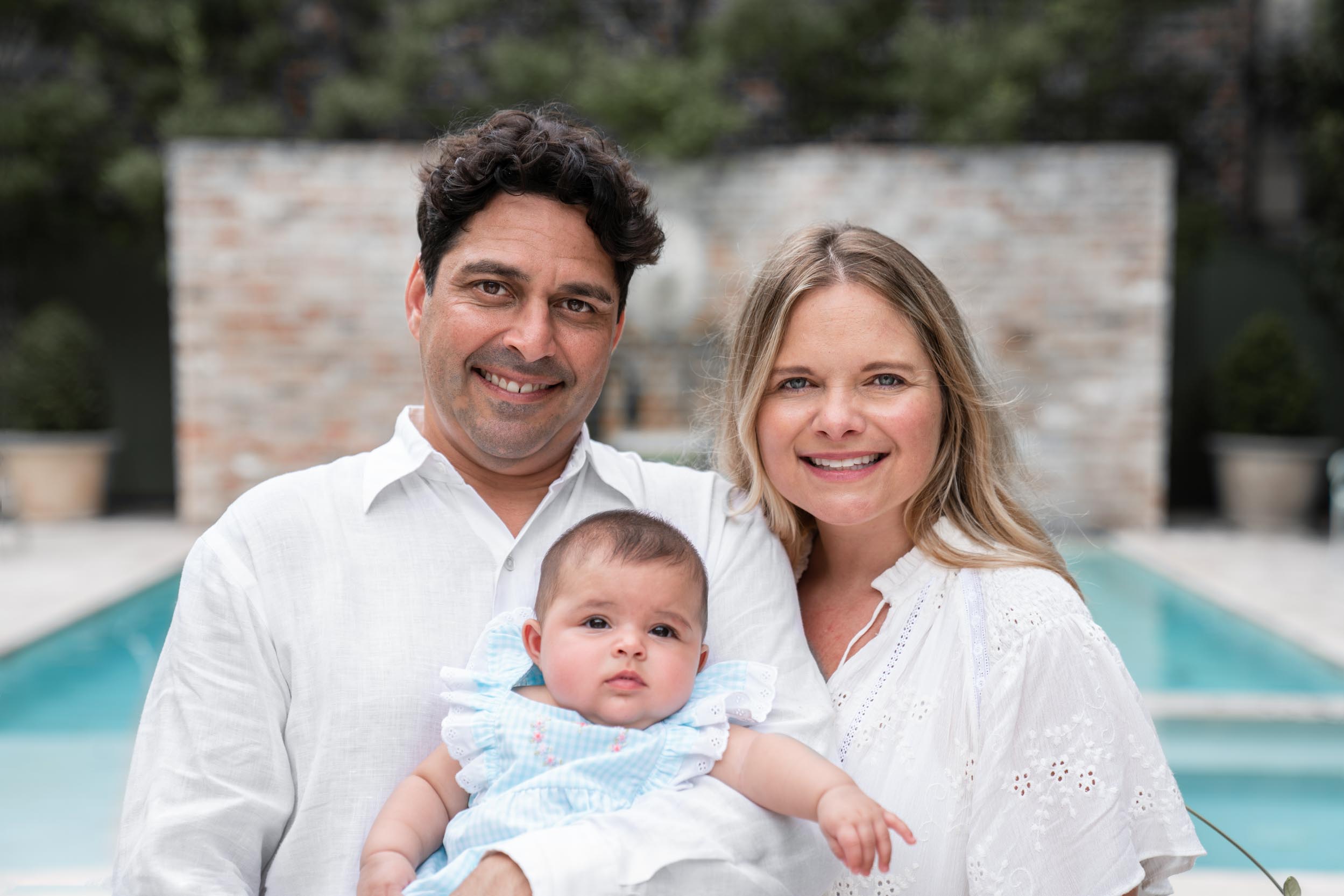 family smiling with baby in front of mansion pool