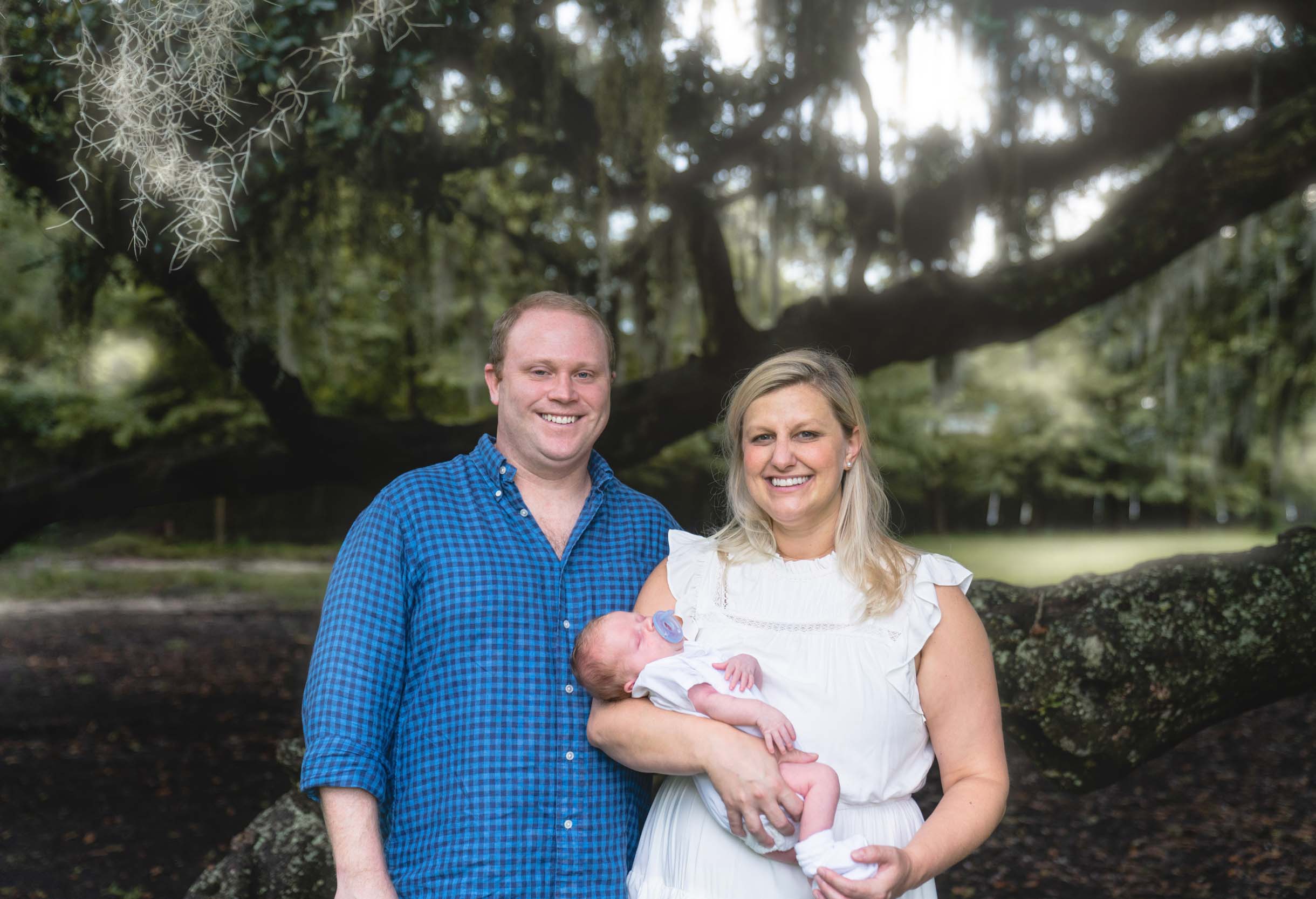 Family with baby smiling in front of oak trees in New Orleans