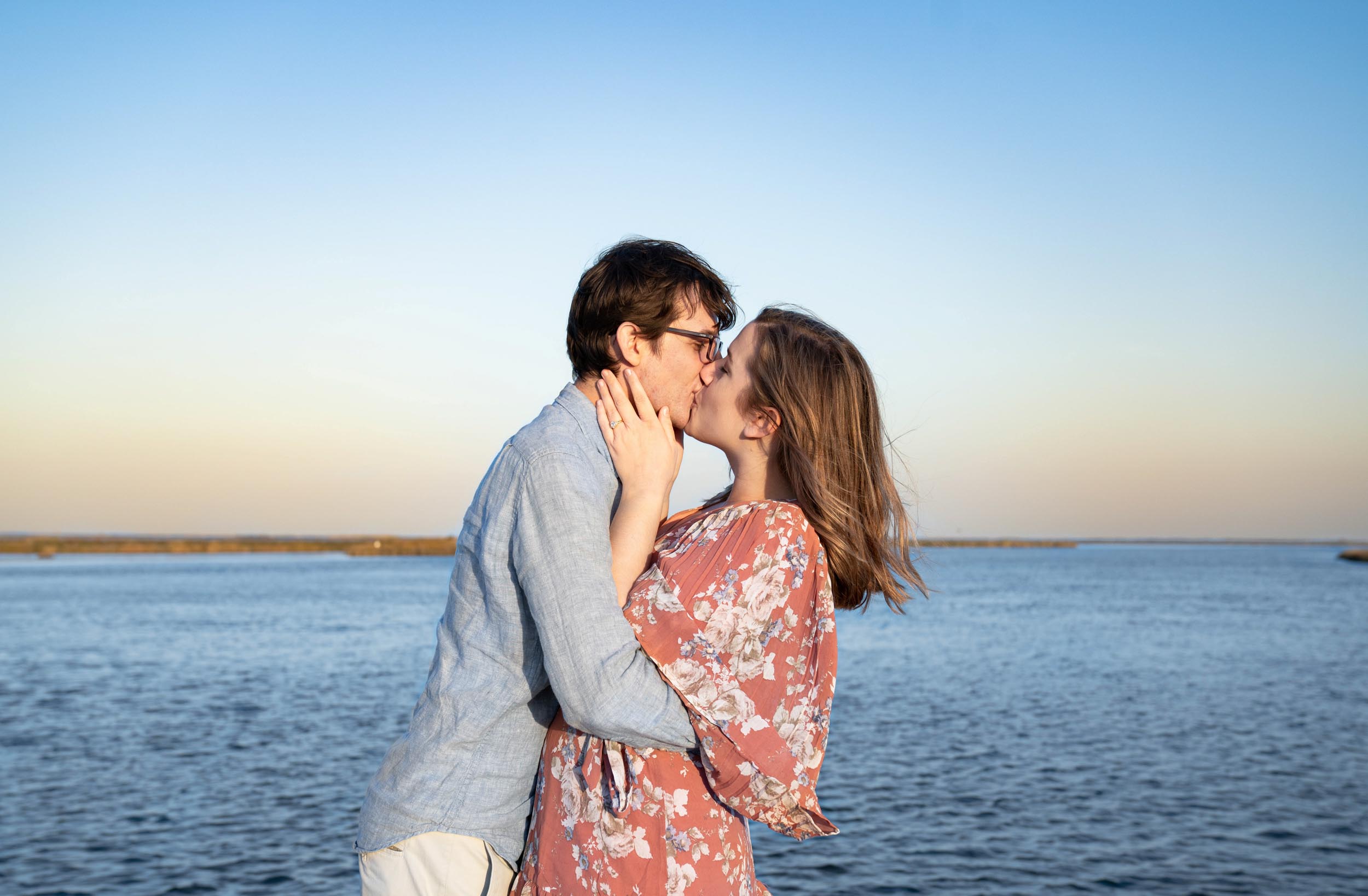 Engaged couple kissing along a bayou vista at sunset in Louisiana after engagement proposal