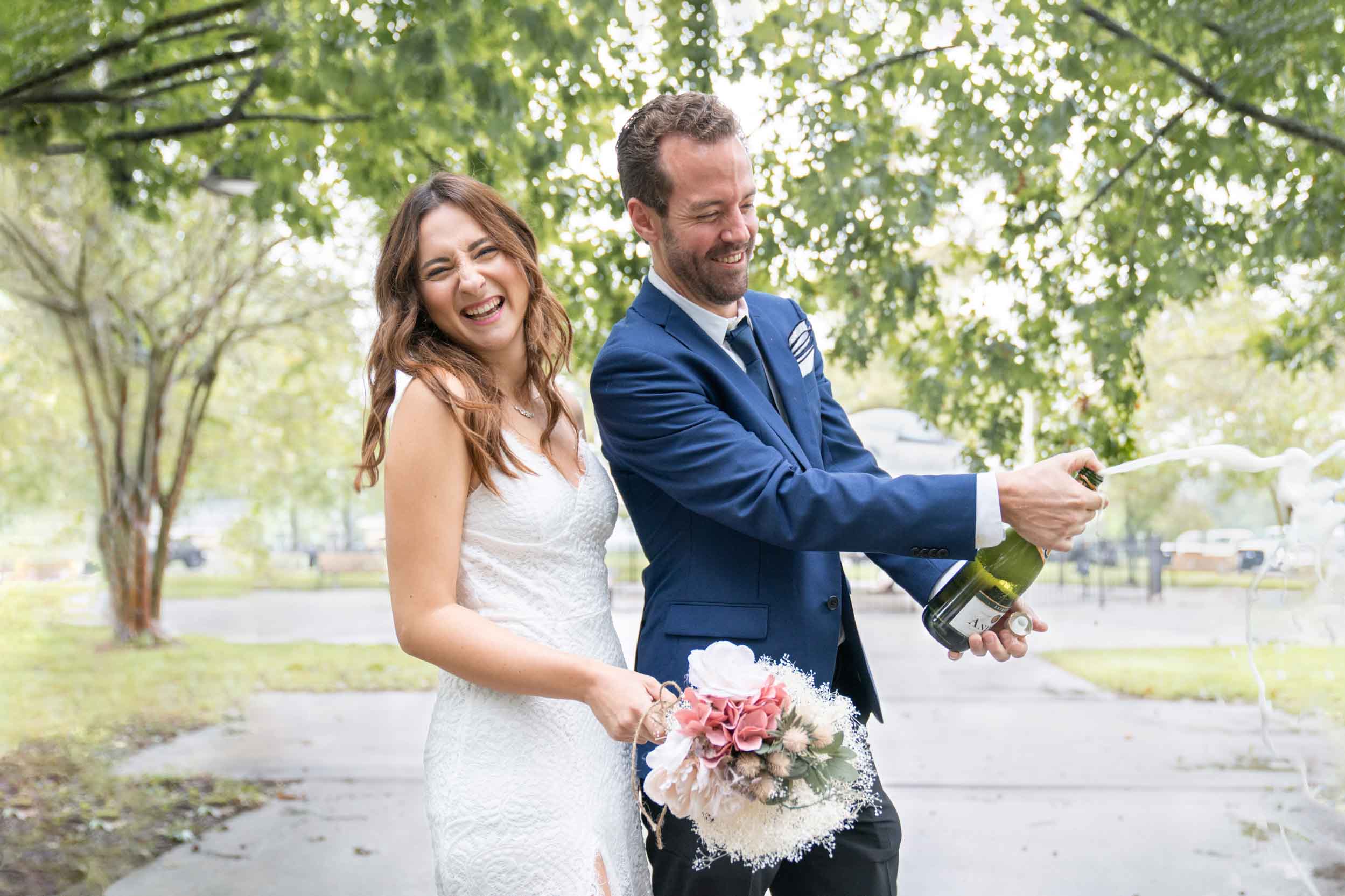 Bride and groom popping a bottle of champagne and celebrating on their wedding day