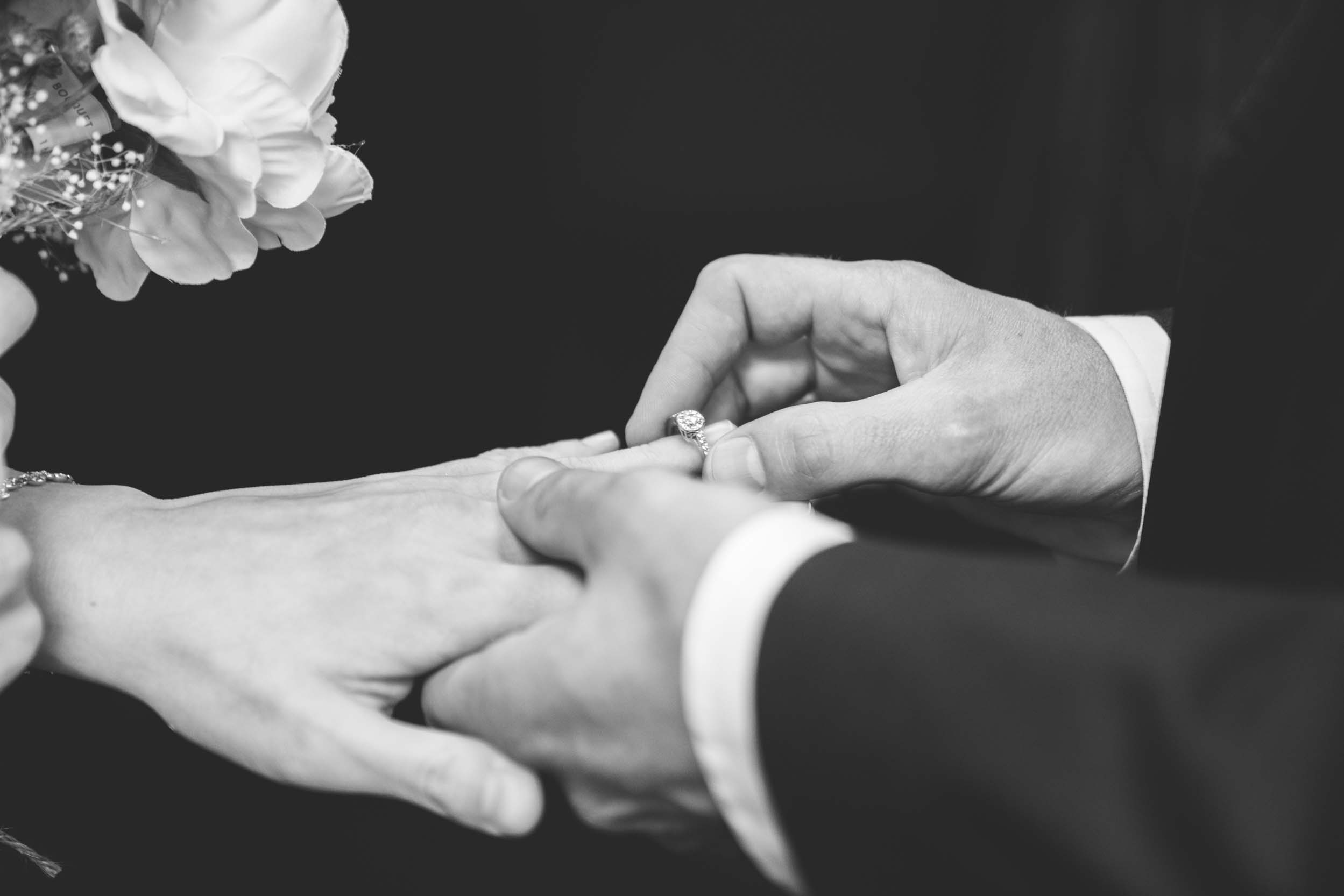 Wedding day of groom placing ring on bride’s finger