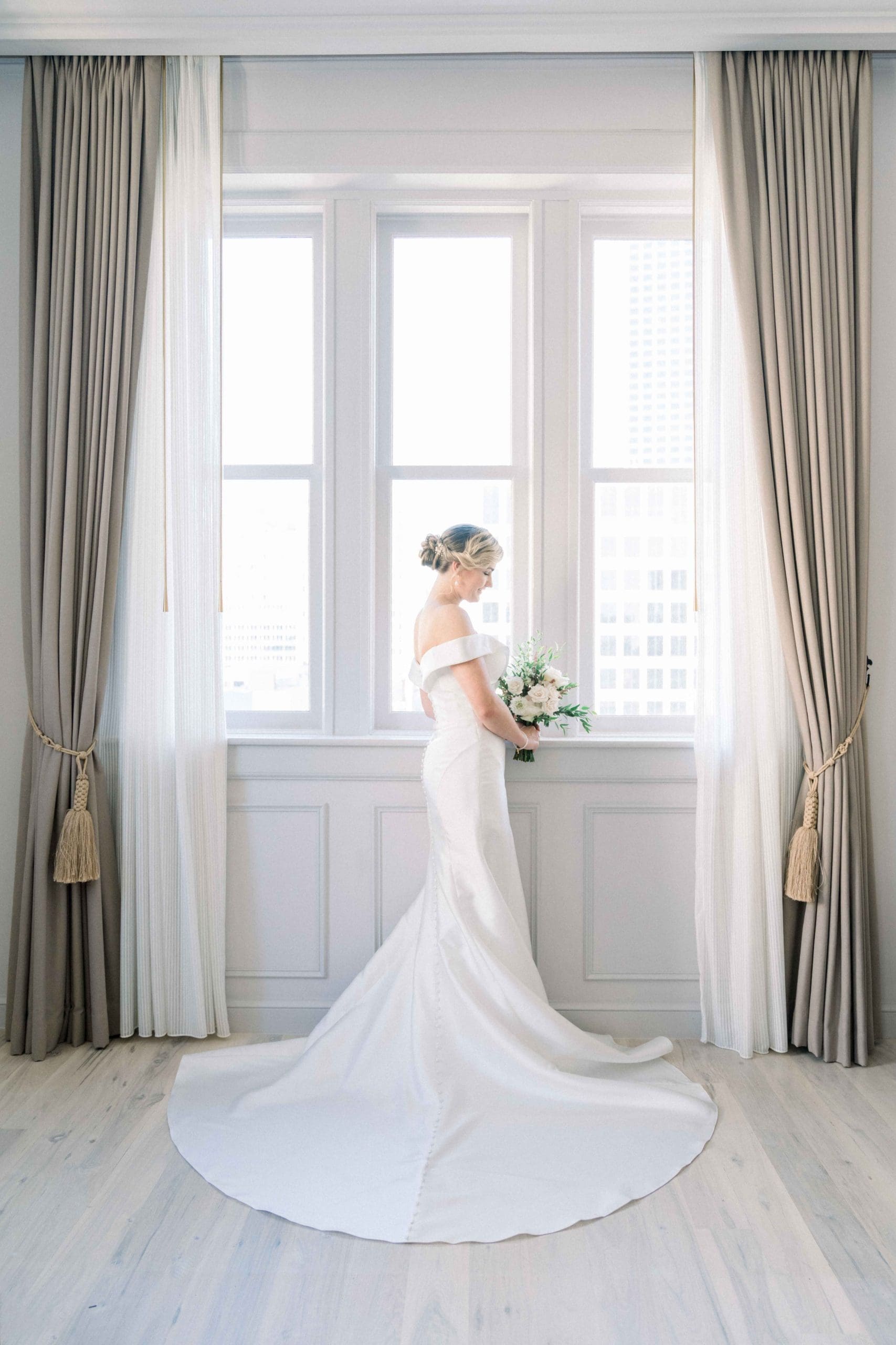 Bride gazing at bouquest in front of window at the Maison De La Luz Hotel in New Orleans