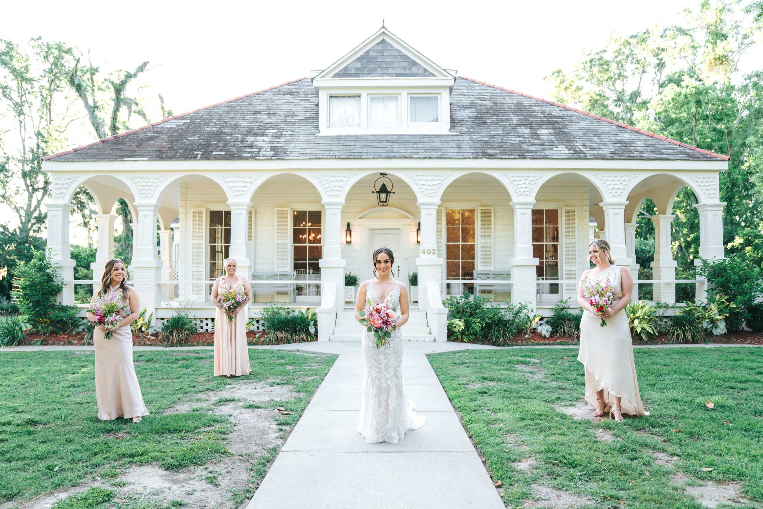 bride and bridesmaids smiling with flowers on front lawn of Maison Lafitte in Covington, Louisiana