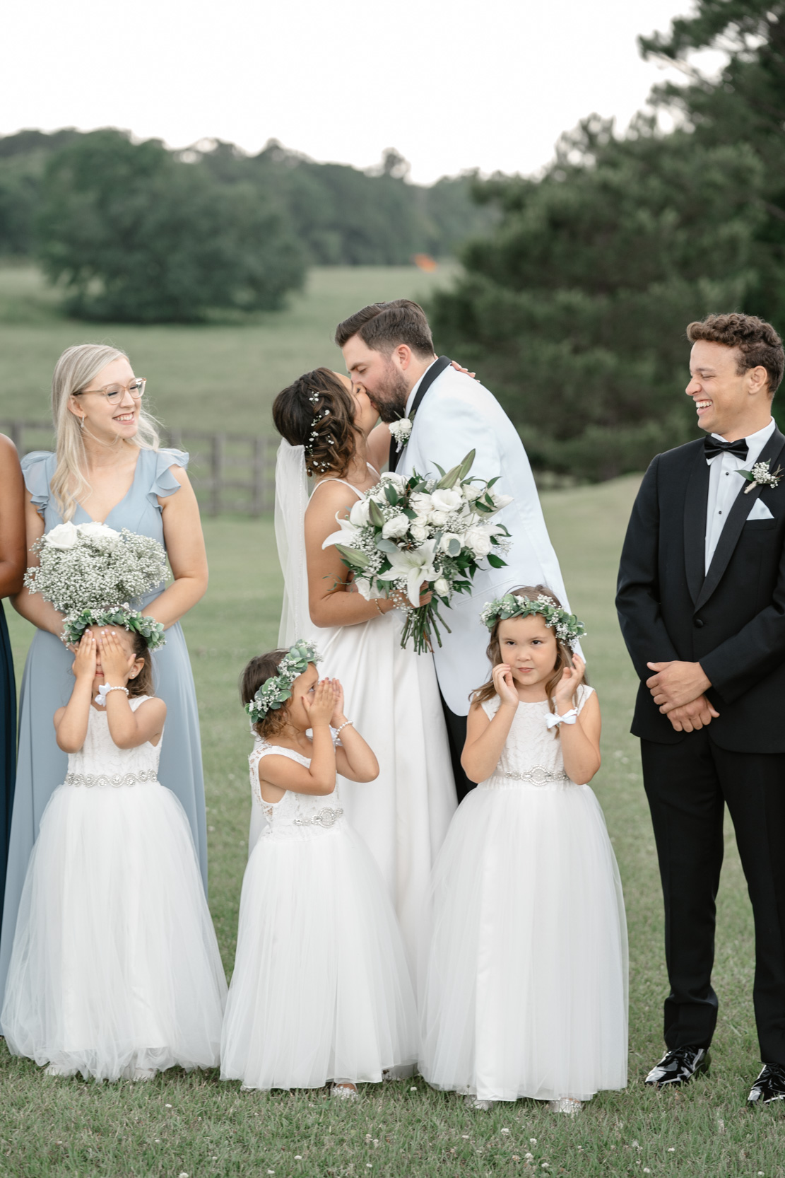 bride and groom kissing in front of children and wedding party at White Magnolia in Louisiana