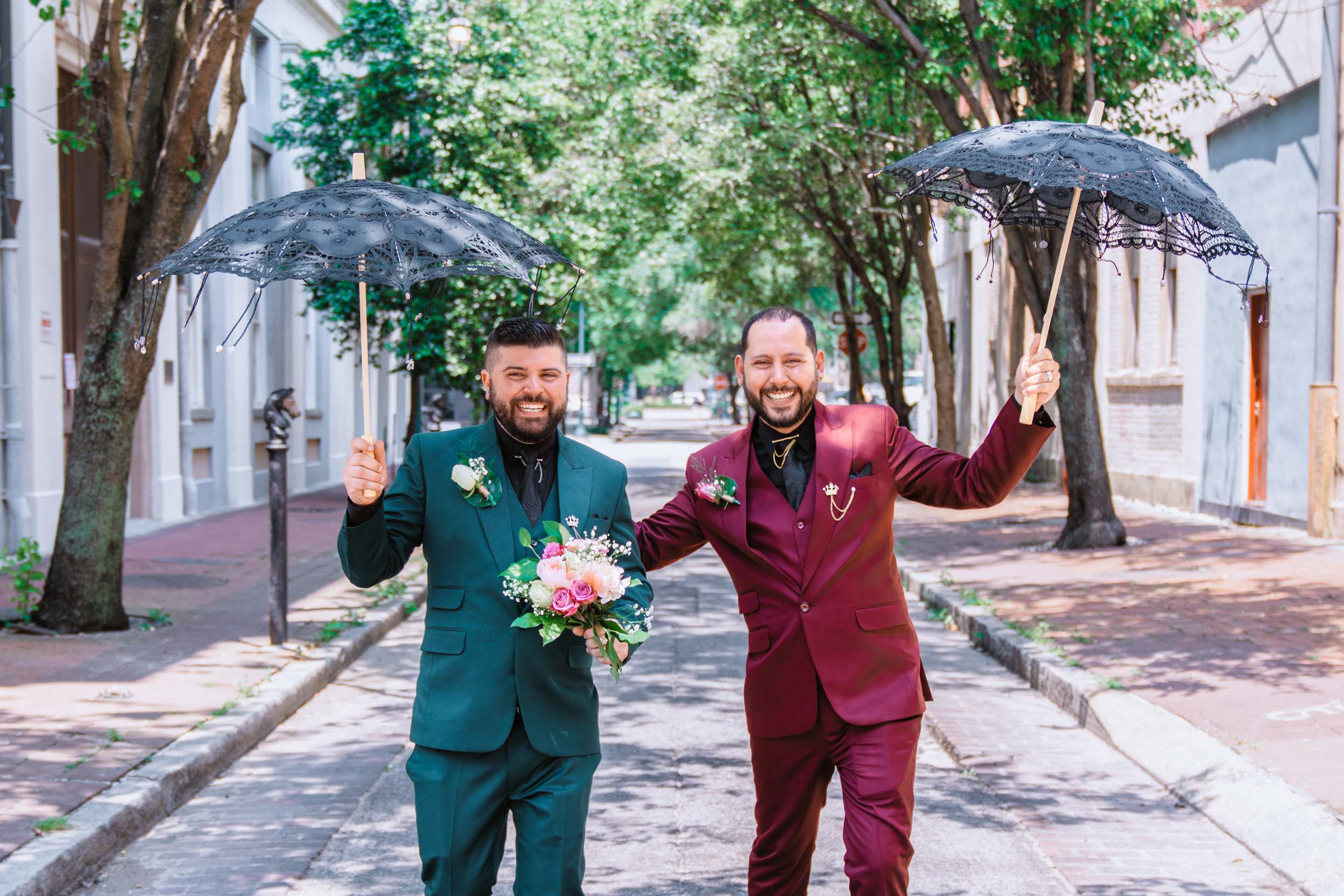 gay couple laughing in street with umbrellas for their elopement in New Orleans