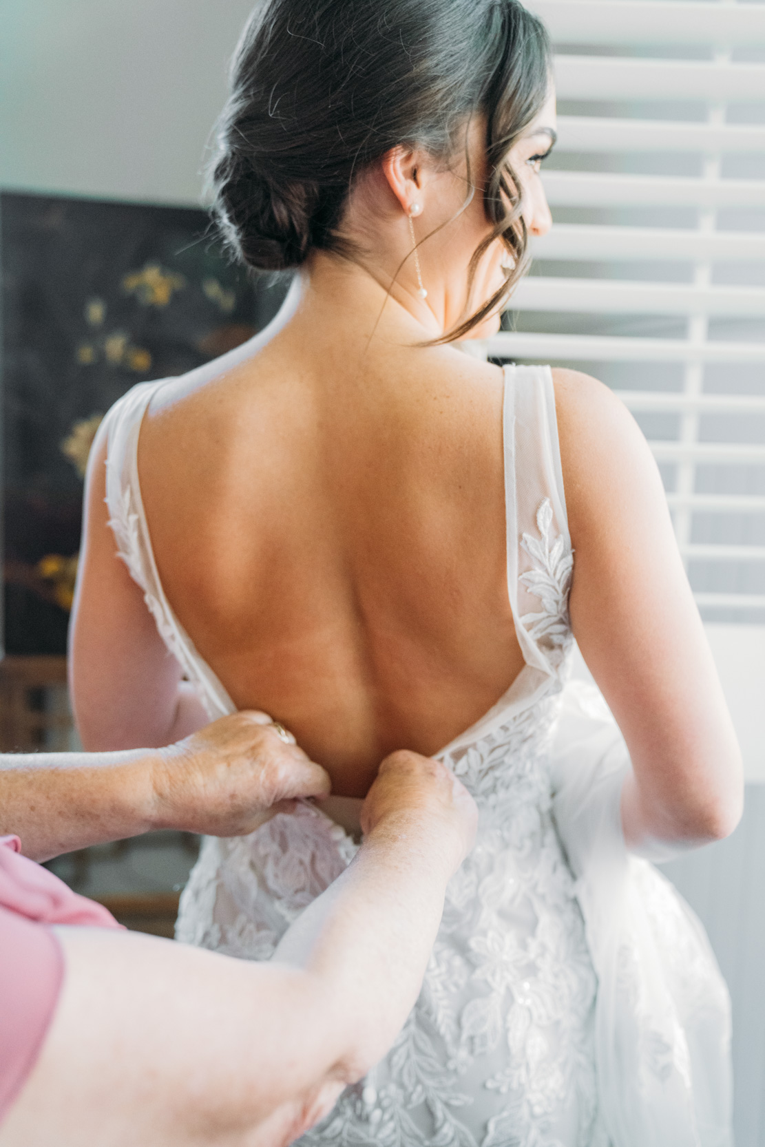 bride getting dressed buttoned up by her mother