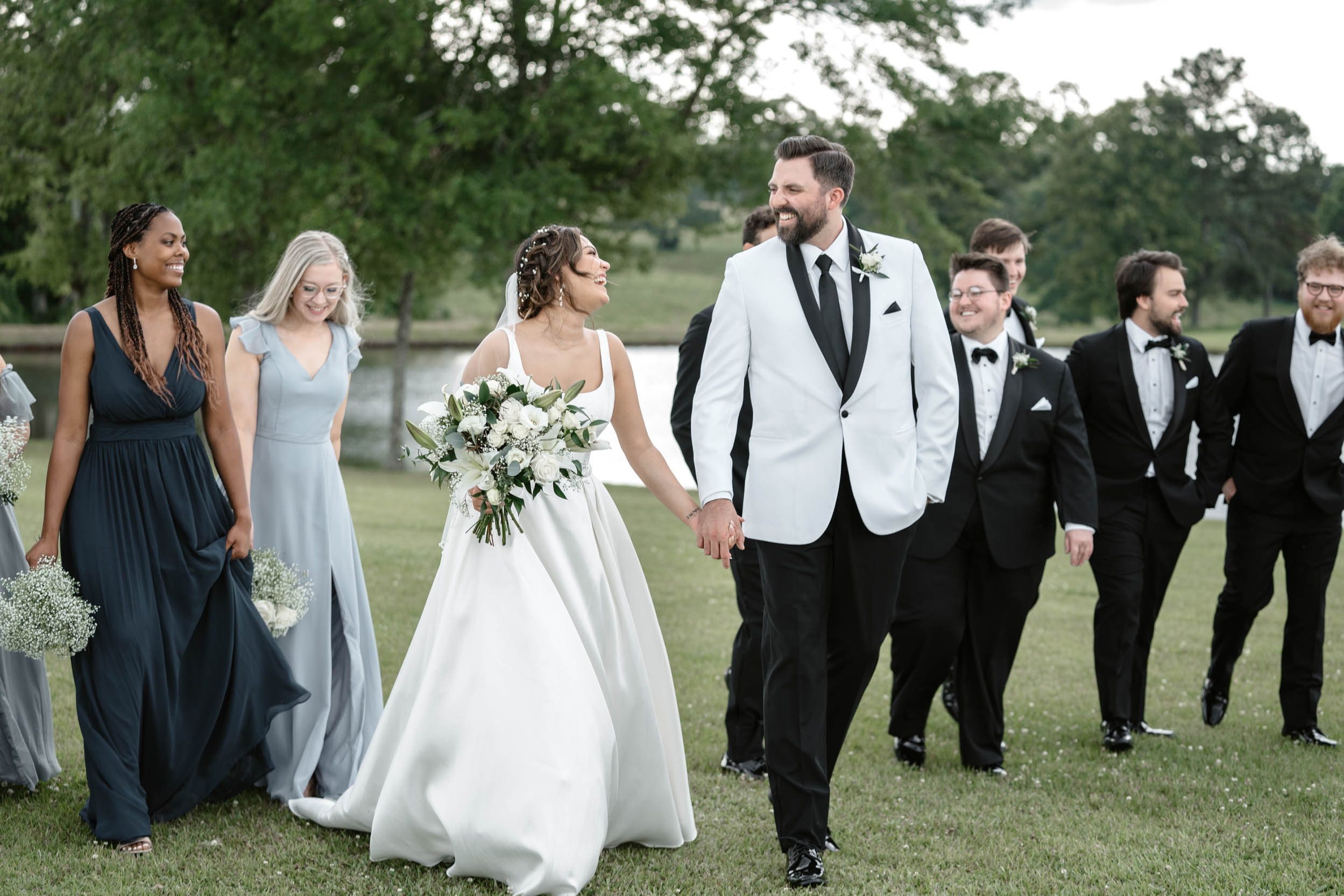 bride and groom laughing in field with wedding party at White Magnolia in Louisiana
