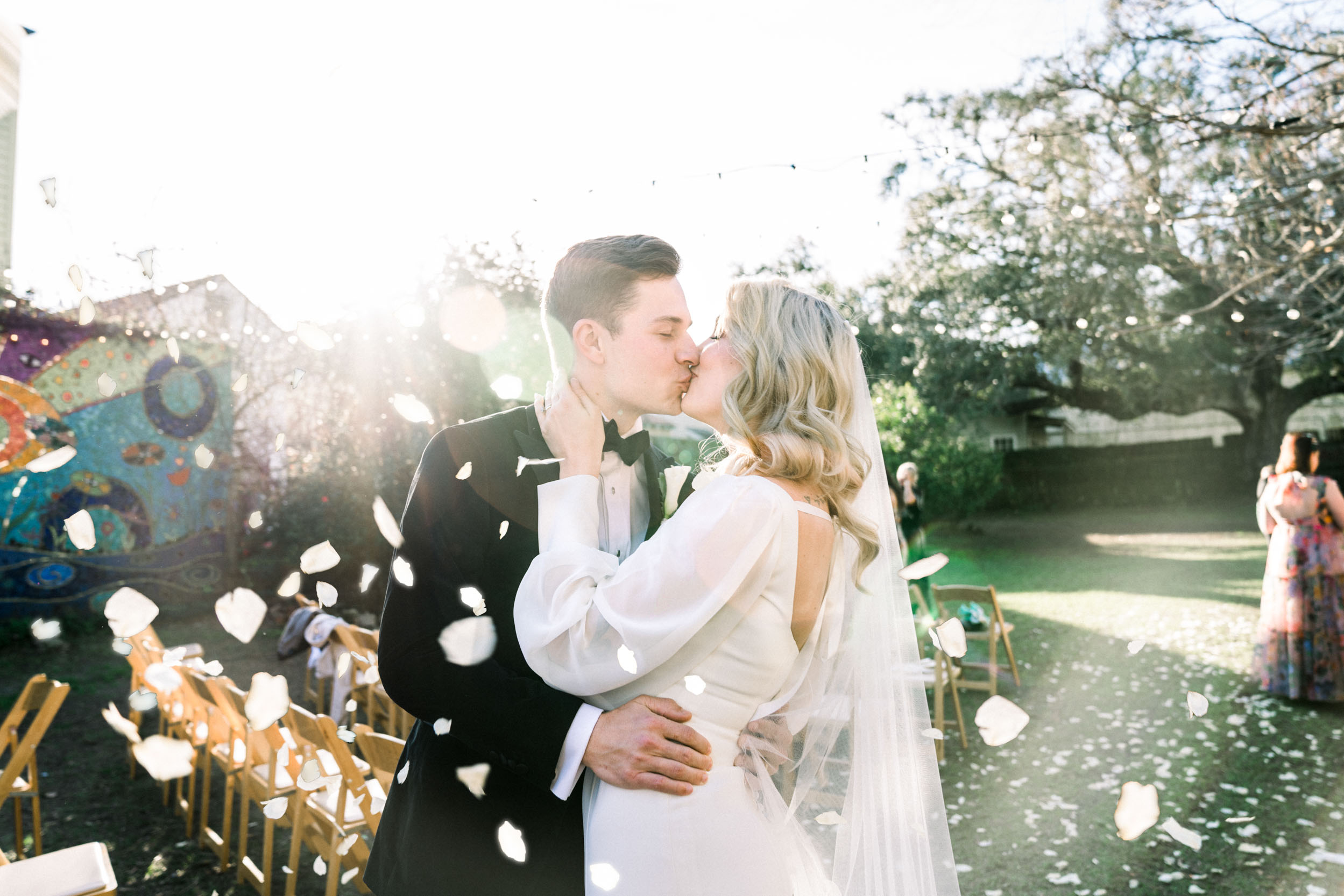 Bride and groom kising with rose petals in the air at Clouet Gardens in New Orleans
