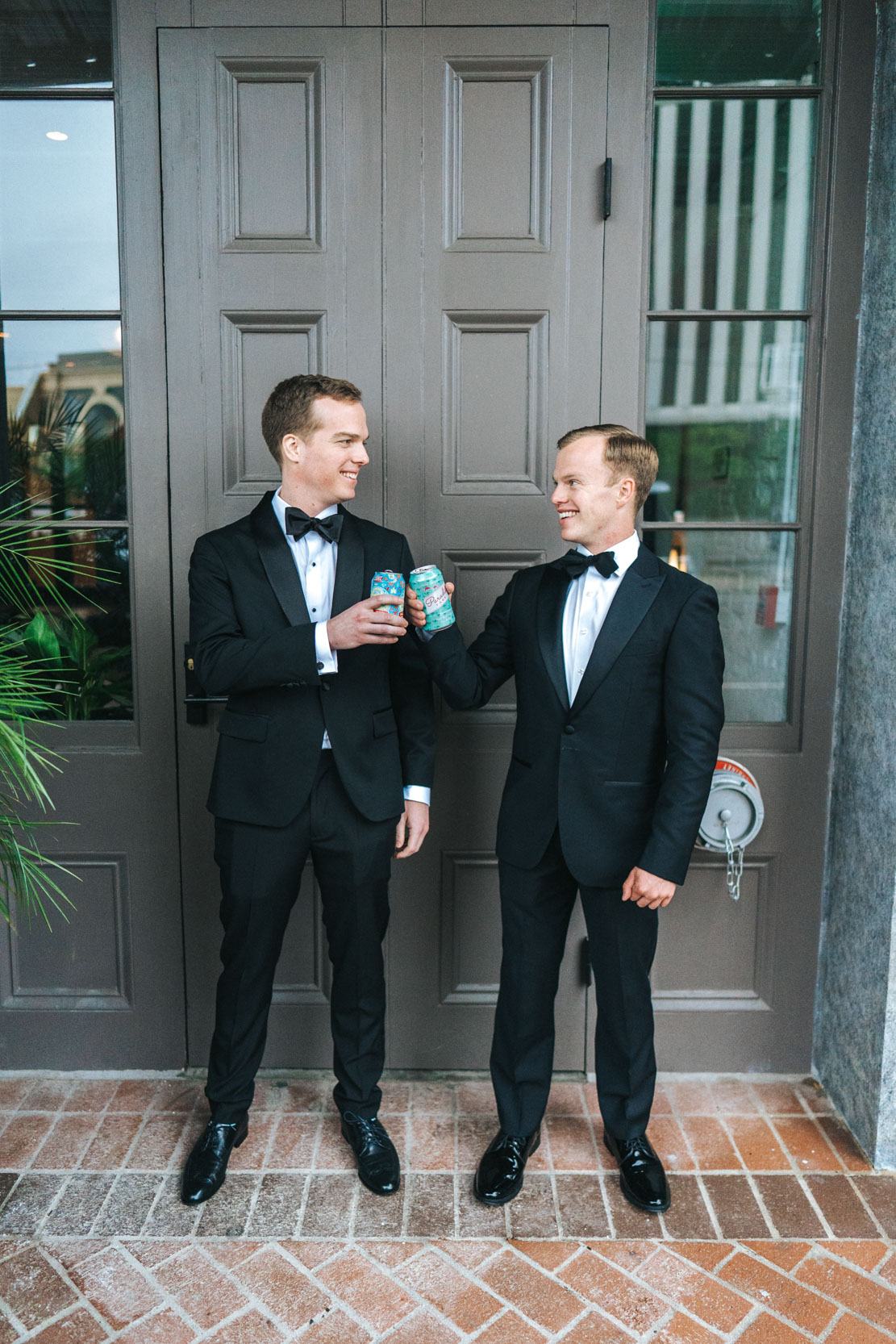 Two groomsmen toasting with a New Orleans beers in front of the Old 77 Hotel