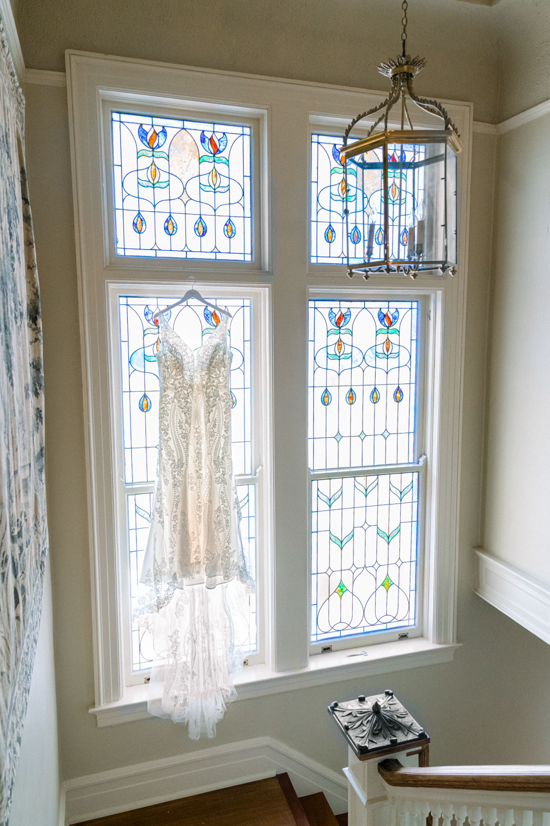 wedding gown hanging in front of stainglass window inside mansion