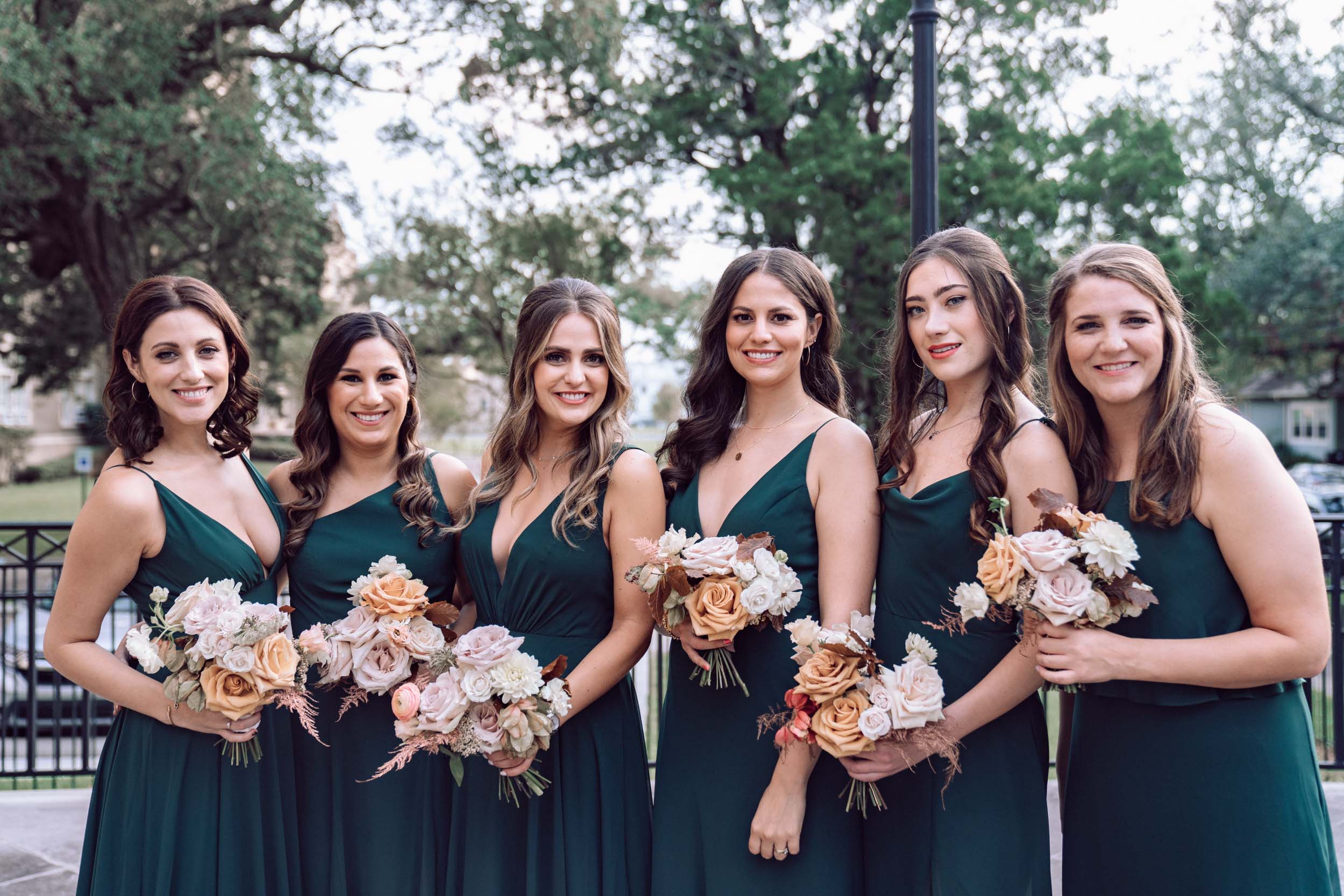 bridesmaids posing with green dresses and flowers and smiling in front of Ursuline Church in New Olreans